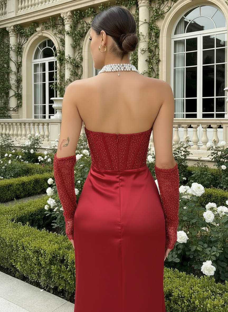 Woman in a red evening gown with open back and long gloves standing in front of an elegant building.